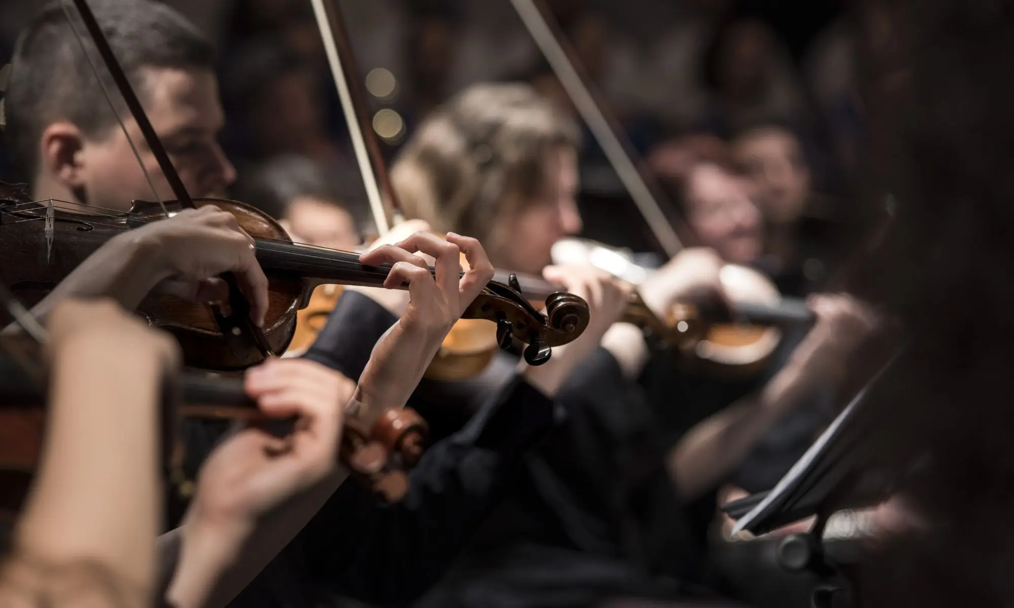 Close-up of musicians playing violins during a live orchestra performance.
